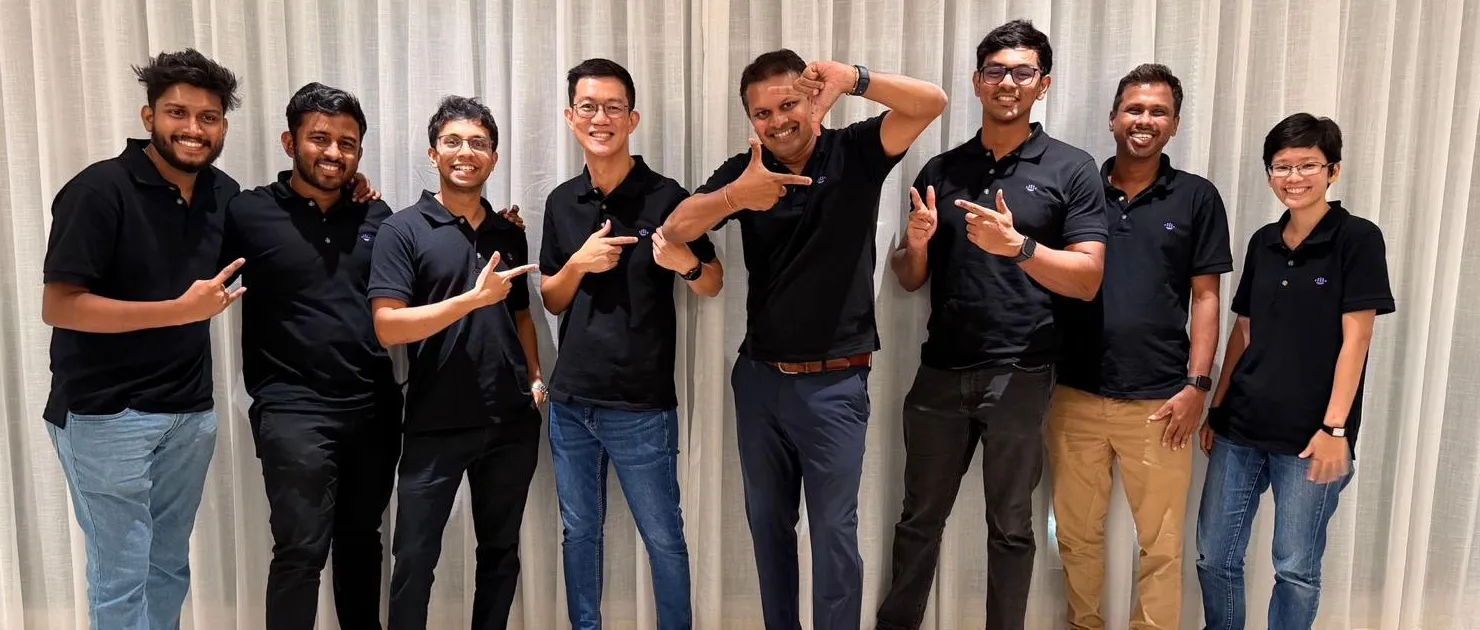 The AiSee team, eight people in matching black AiSee polo shirts, smiling and posing together in front of a white curtain.